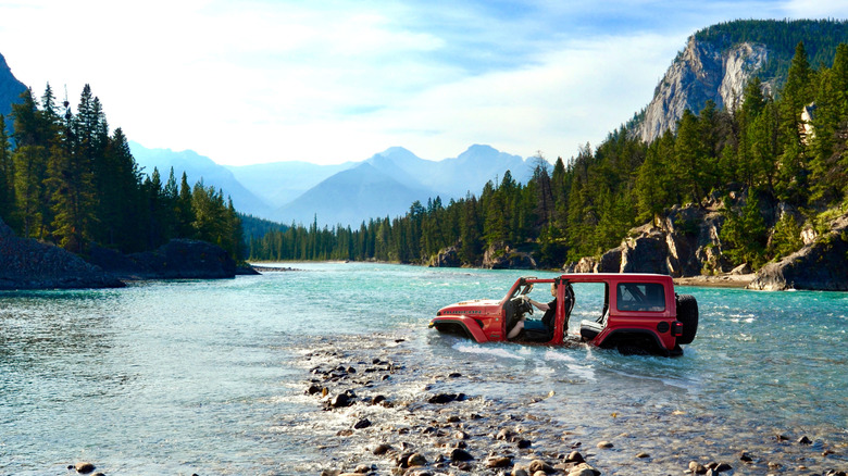 An Orange, 2025 Jeep Wrangler Unlimited fording its way through a riverbed in the mountains that was before Stellantis started using Ai for imagery.