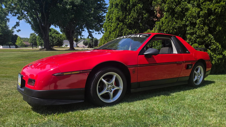 A red, 1984 Pontiac Fiero on a green lawn.