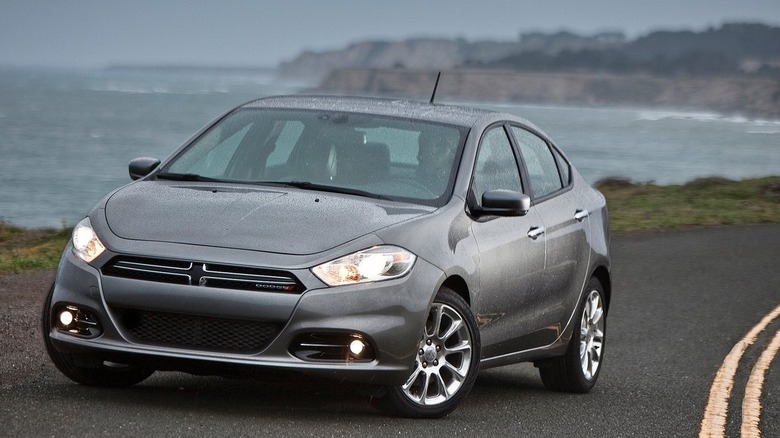 Front three quarters shot of a silver Dodge Dart parked on a road in front of cliffs and the sea