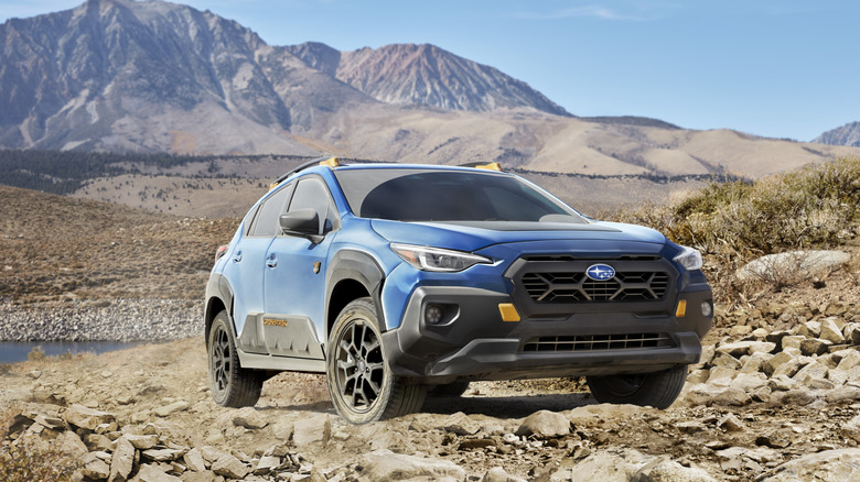 Front three quarters shot of a blue Crosstrek WIlderness parked on rocks  in front of a mountain range in the desert