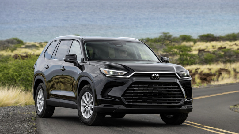 A toyota highlander parked on the side of the road in front of some dunes and water