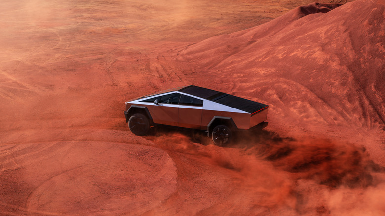 The drastically angular and annoying steel covered Tesla Cybertruck driving about in red sand which is either supposed to be Mars-like or hell-like.