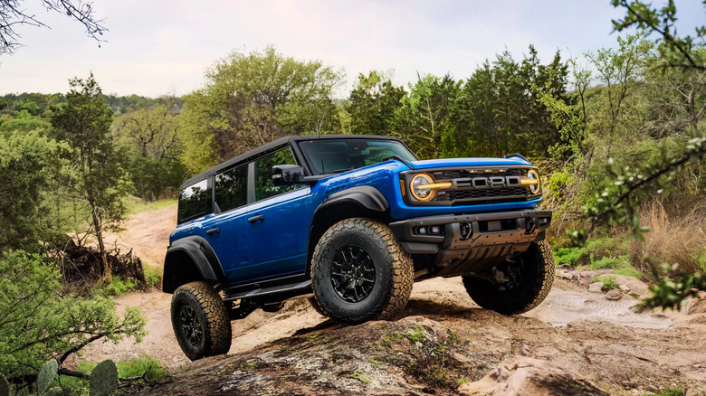 A blue Ford Bronco Raptor tackles a rocky and muddy terrain.