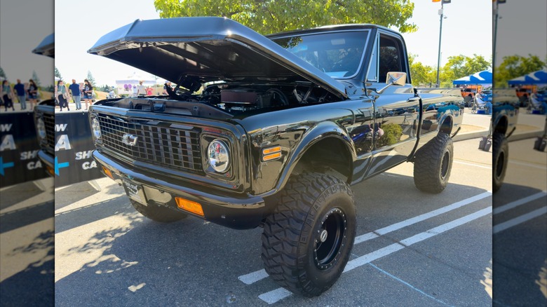 A very lifted black C10 Chevrolet pickup truck at what looks like to be a car show parking lot.