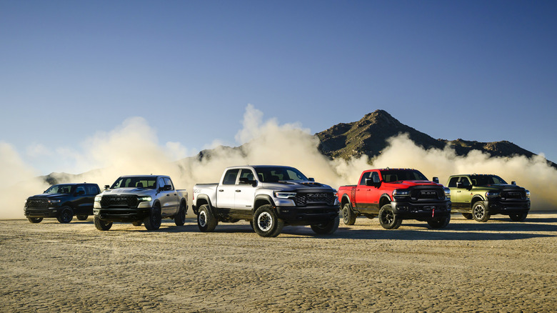 A small fleet of five obnoxiously large RAM pickup trucks in a desert setting with dust kicked up behind them like they ran around and parked.