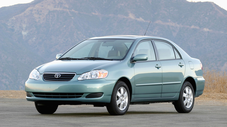 Front three-quarters shot of a light blue/green 2003 Corolla parked in front of a mountain