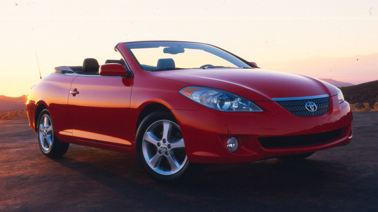 A front three-quarters shot of a red Solara convertible with its top down parked in front of a view of a sunset