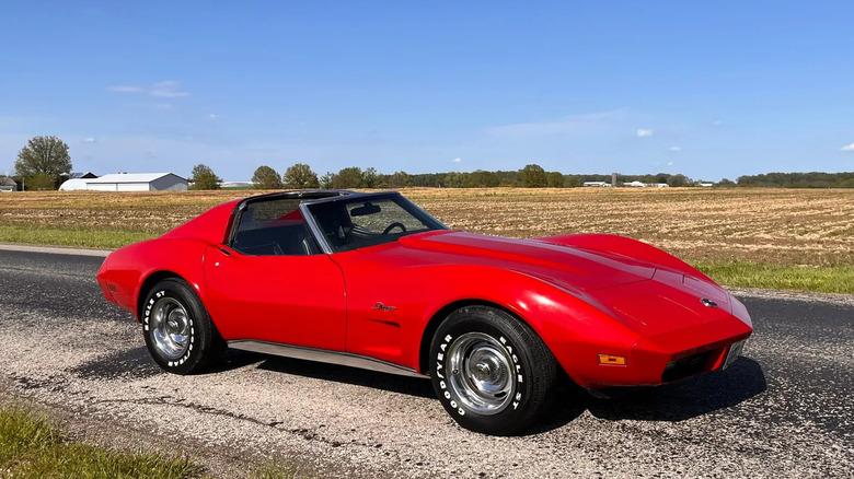 A red 1974 Chevrolet Corvette on a country road with a bare farm behind it.