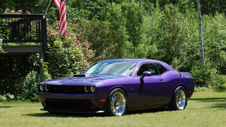 A purple, Dodge Challenger on the grass of someone's backyard with gaudy tires.