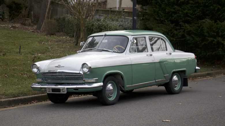 A green and white Gaz Volga parked on the side of a neighborhood road.