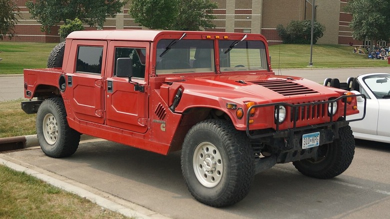 A red Hummer H1 in a parking lot near some form of university structure.