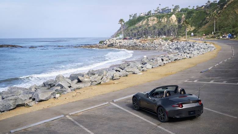 Mazda Miata MX-5 in grey at a seaside parking lot, overlooking rocks and the water.