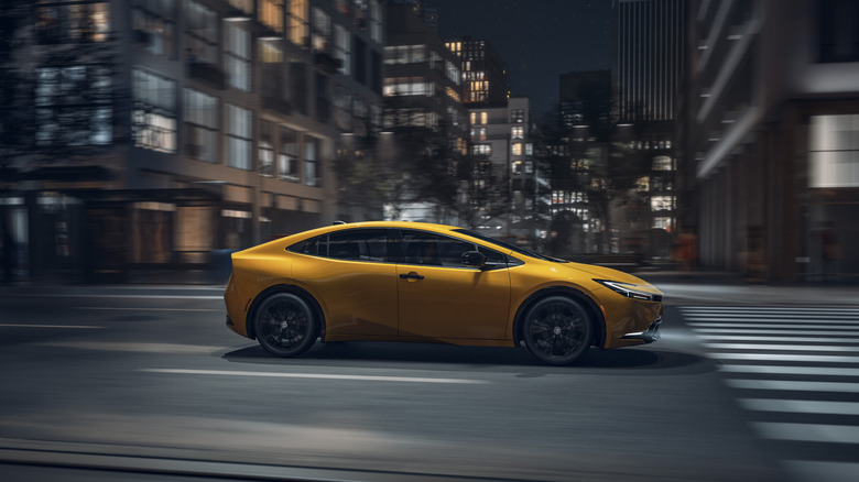 A sexier Toyota Prius, 2027 model in Nightshade which is a golden yellow, driving on city streets in the evening.