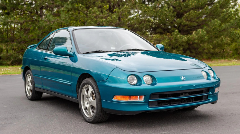 A prime teal 1994 Acura Integra GS-R coupe with pinstriping, parked on a blacktop with a tree line in the background.