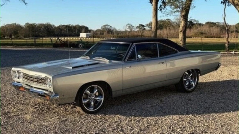 Silver 1968 Plymouth Roadrunner 383 with black sim top in a gravel parking area.