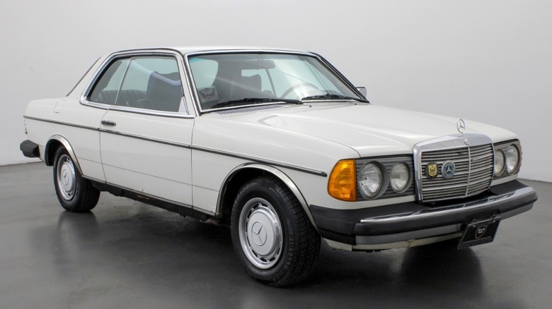 A white 1978 Mercedes 300CD two-door in a plain photo studio with grey flooring and white walls.