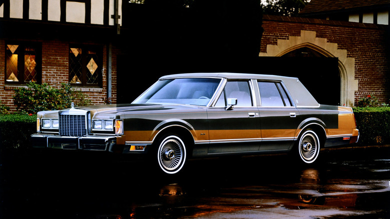 A gold 1988 Lincoln Town Car sits in front of a beautiful brick estate, with a small black overlay of a black 1988 Lincoln Town Car with grey cloth sim roof.