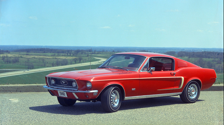 A beautiful red 1968 Ford Mustang GT fastback parked with a scenic grassy background.