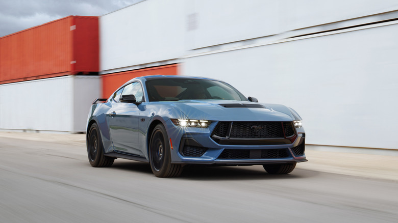 A blue Ford Mustang GT driving long a row of stacked shipping containers