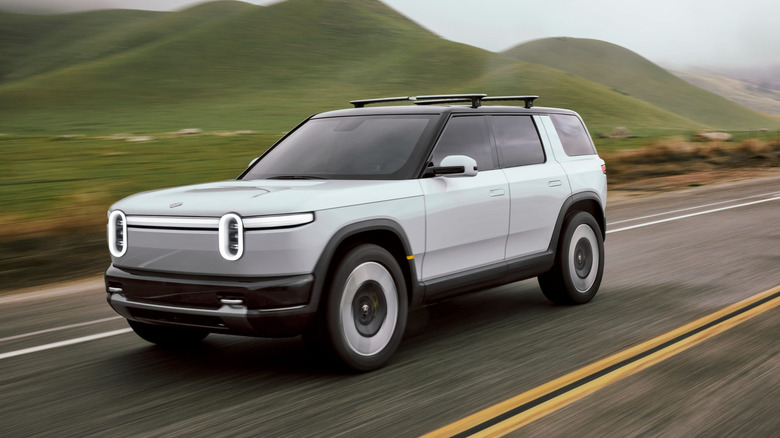 A white Rivian R2 driving down a two-lane highway