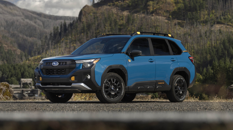 A blue Subaru Forester Wilderness on a gravel road with a mountainous backdrop