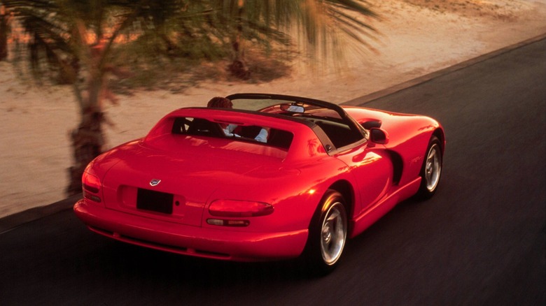 rear three quarters shot of a red Viper driving down a road next to sand and a palm tree