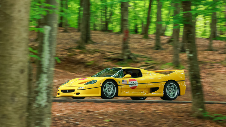 A yellow Ferrari F50 driving through a forest past trees and detritus