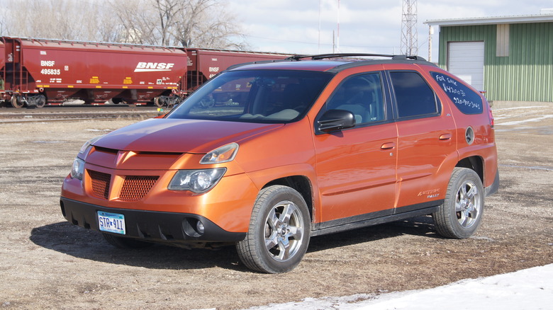 An orange 2005 Pontiac Aztec with a freight train passing in the background