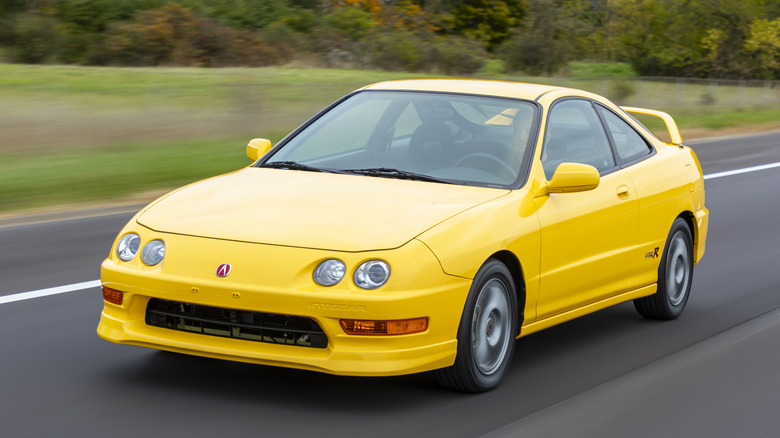 Front three quarters shot of a bright yellow Acura Integra Type R driving past trees and grass