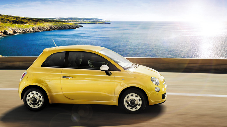 A side view of a bright yellow 500 driving on a seaside road