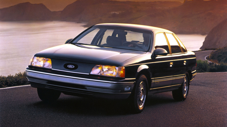 Front three quarters shot of a black first-gen Taurus driving on a seaside cliff road at dusk
