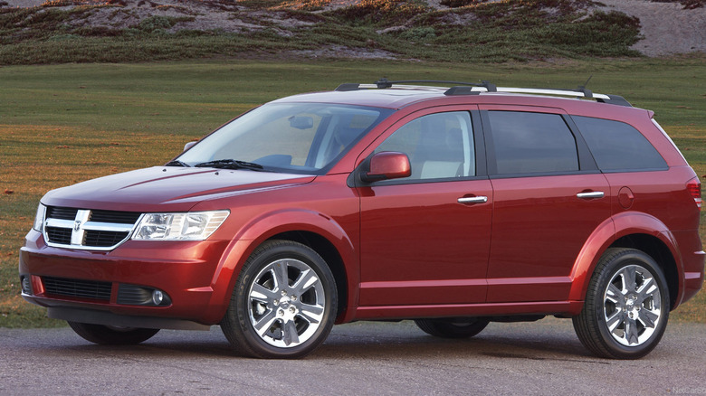 Front three-quarters image of a red Dodge Journey parked on gravel in front of grass