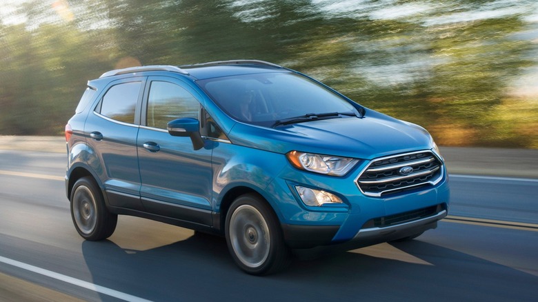 Front three-quarters image of a blue EcoSport driving on a two-lane road past blurred trees