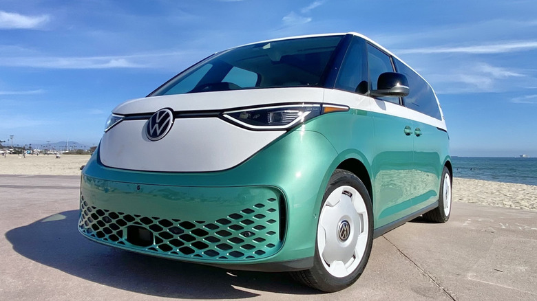 front three-quarters image of a green and white ID Buzz parked on concrete at the beach in front of a slightly cloudy blue sky and the ocean