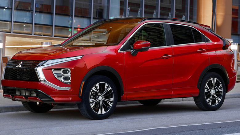 Front three-quarters image of a red Mitsubishi Eclipse Cross parked on a street in front of a building with lots of windows