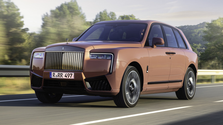 Front three-quarters image of a "Morganite" Cullinan driving on a highway past trees and a metal guardrail