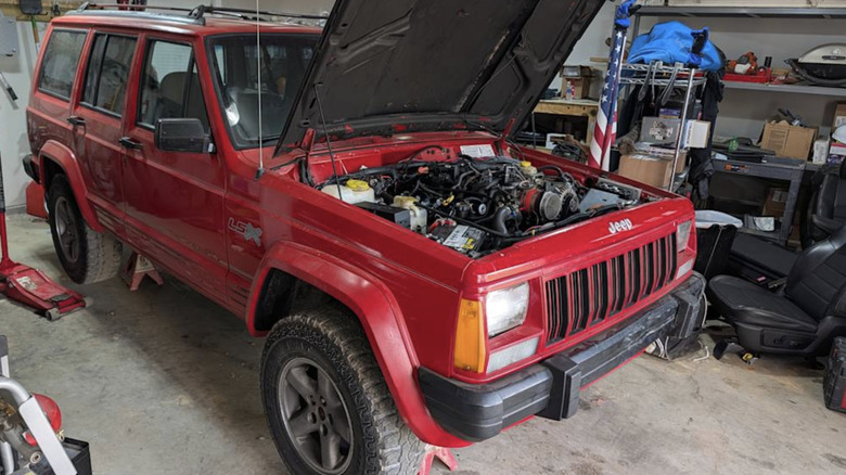 a red jeep XJ with the hood open and an engine visible inside