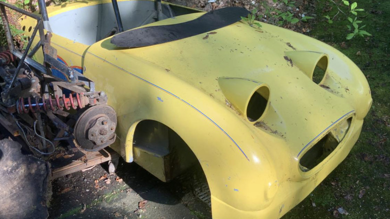 A yellow Sprite shell with no wheels or seats. The engine is sitting next to it