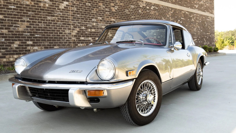 Front three quarters shot of a silver Triumph GT6 Mk III parked in front of a brick wall