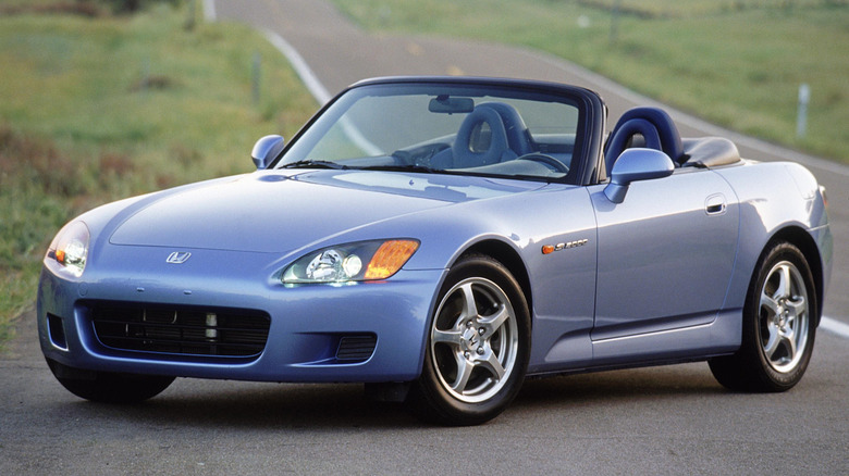 A front three quarters shot of a periwinkle S2000 with its top down parked at the side of a two-lane road lined with grass