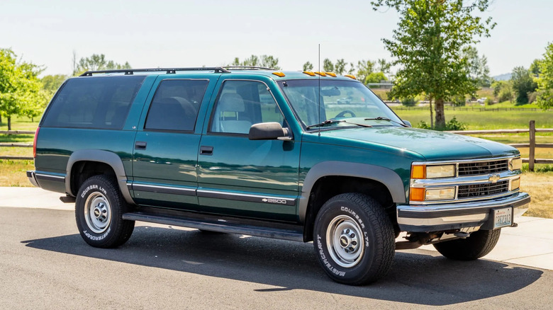 A front three quarters shot of a green GMT400 Suburban parked in front of grass and trees