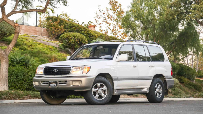 Front three quarters shot of a white Land Cruiser parked in front of a plant-covered embankment
