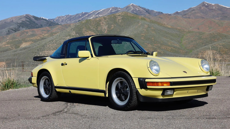 Front three quarter shot of a yellow Porsche 911 Targa parked in front of a mountain range
