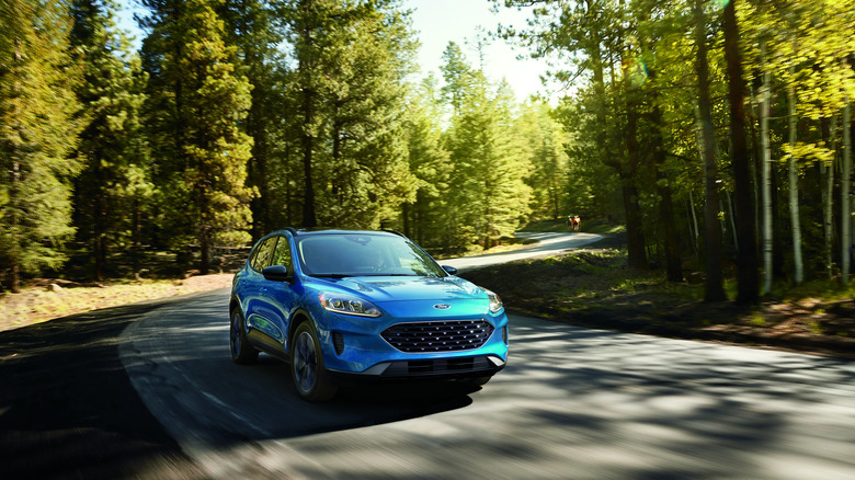 A blue Ford Escape driving around a corner on a windy street lined with trees