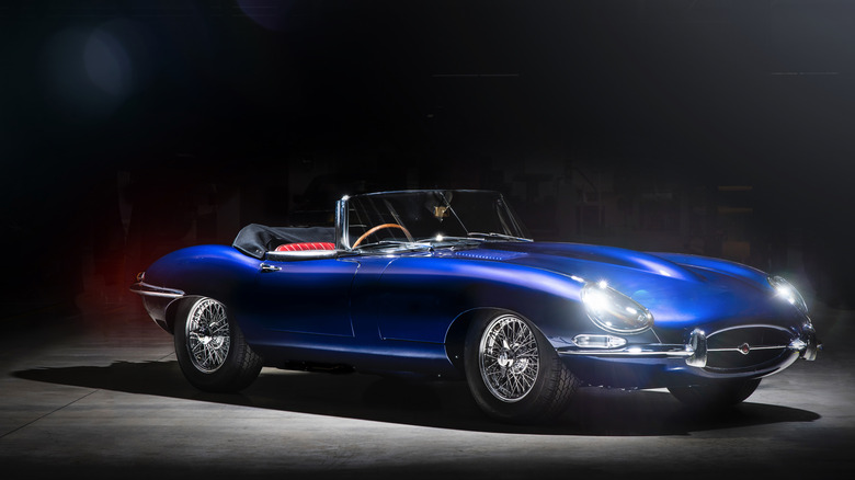 A blue Jaguar E-type convertible with its headlights on, shot in a dark studio