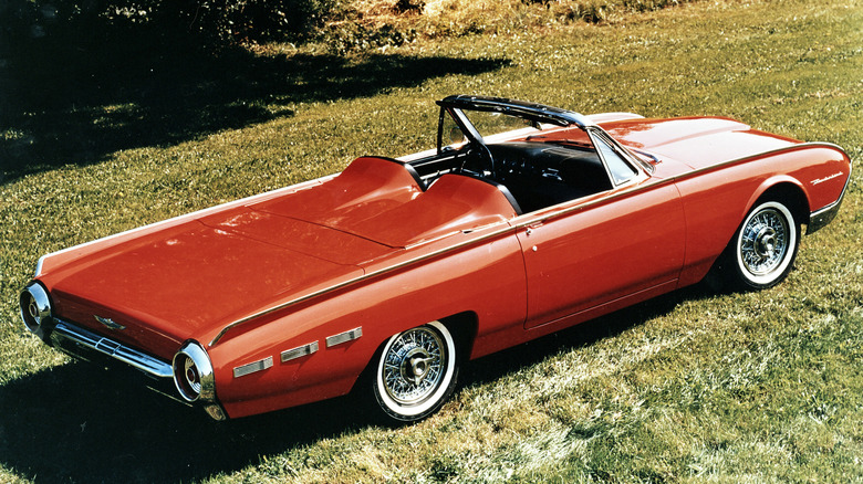 A red 1963 Ford Thunderbird Sports Roadster with its roof down, shot from a slight elevation over the rear three quarters. The car is parked on grass