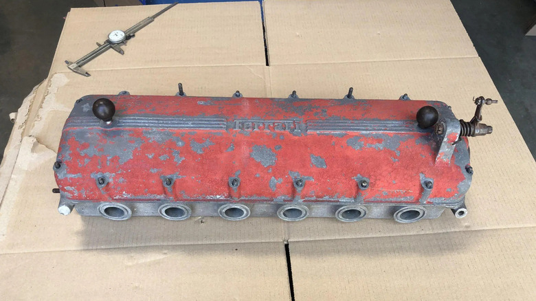 A distressed red magnesium Ferrari valve cover sitting on a cardboard box