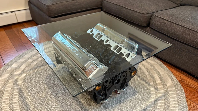 An overhead shot of a coffee table made out of a small block chevy V8 in front of a couch on a rug