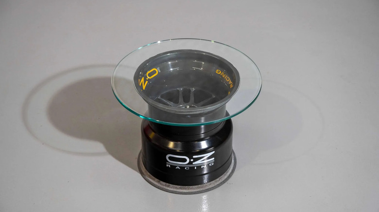A wheel table made of an OZ Racing wheel sitting upright with a glass circle on top