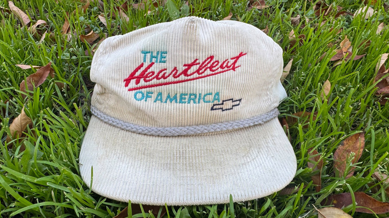 A photo of my white corduroy Heartbeat of America hat sitting on grass with brown leaves surrounding it